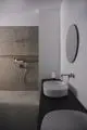 Badezimmer mit Dusche, gefliestem Wandbereich aus grauem Material und ovalem Waschbecken. Ideal Standard Sanitärarmaturen an Wand montiert. Spiegel an der Wand.